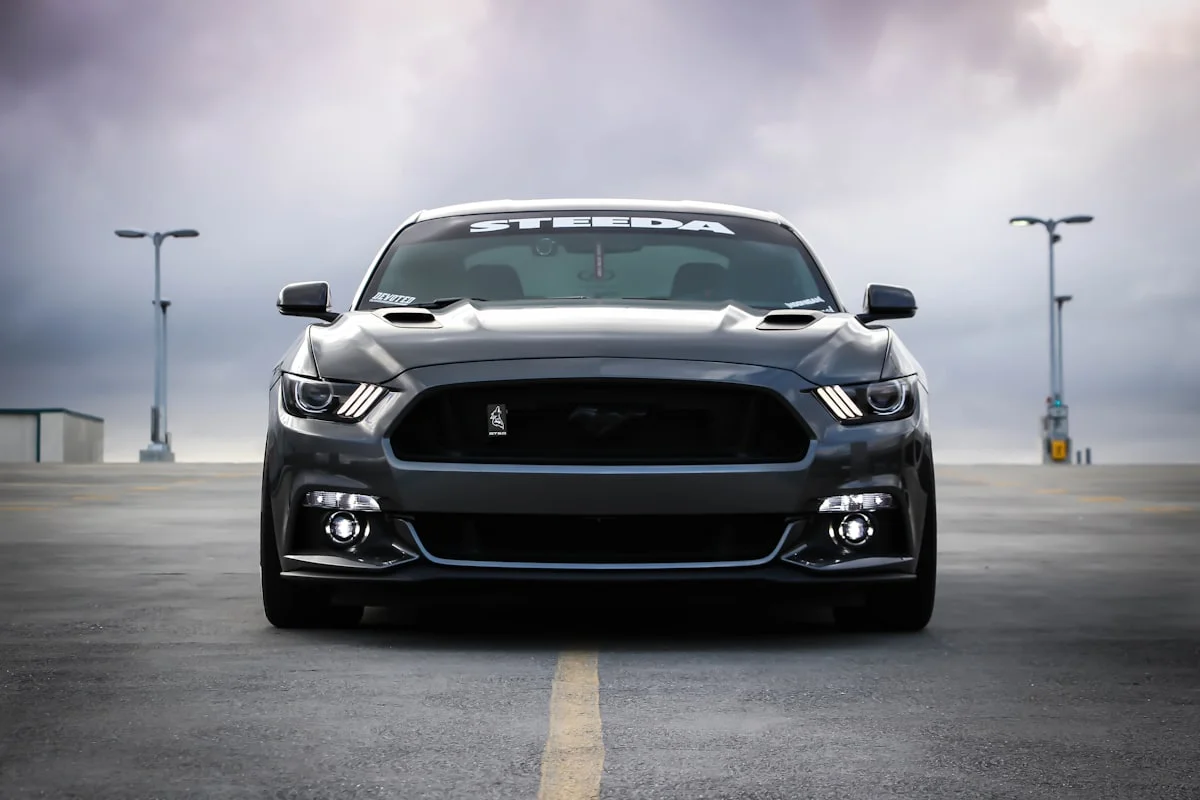 Grey Ford Mustang coupé photographed head-on across an empty rooftop car park under heavy cloud.