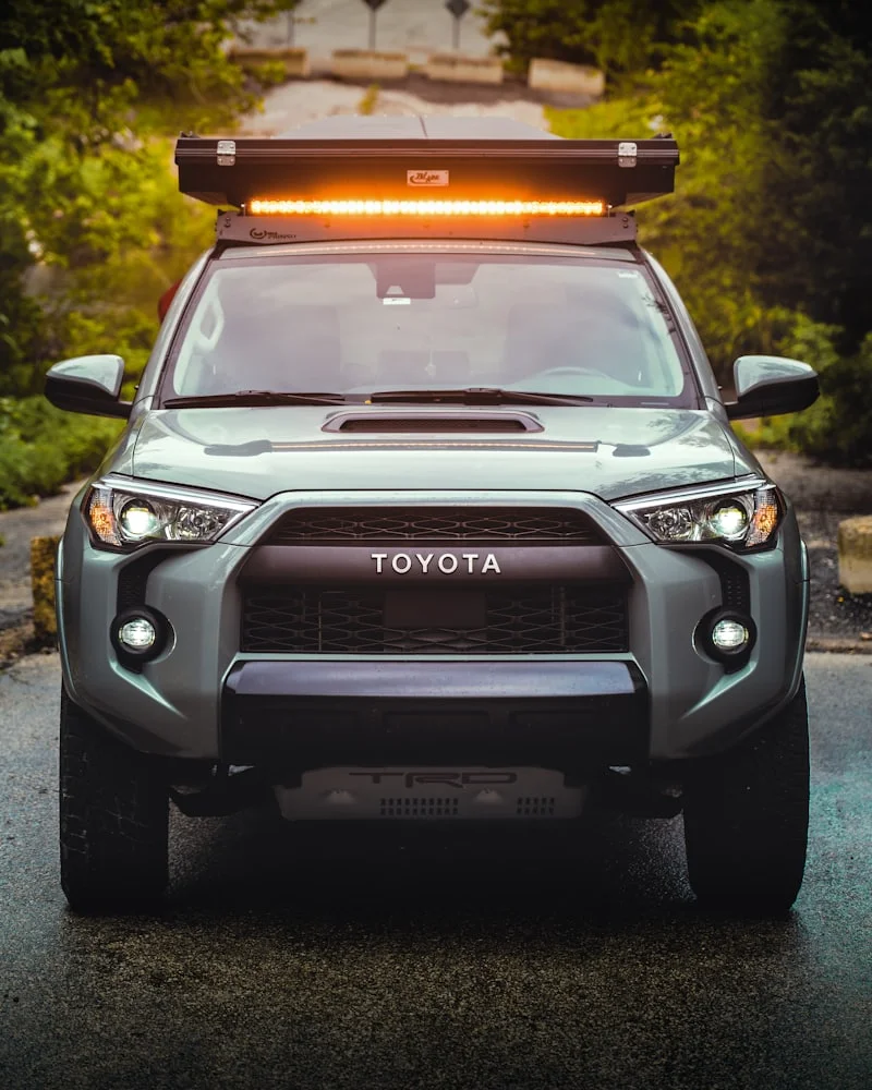 Grey Toyota 4Runner photographed head-on at dusk, fitted with a roof rack and a light bar.